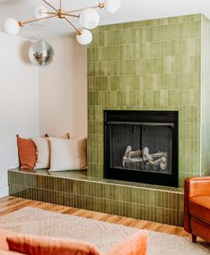 a living room with a fire place in the center and green tiles on the wall