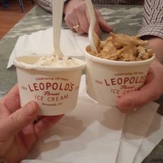 two people holding up ice cream cups with toppings on them, while sitting at a table