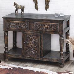 an old wooden table with two horse figurines on top and a cowhide rug in the corner