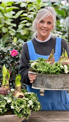 an older woman is holding up some plants