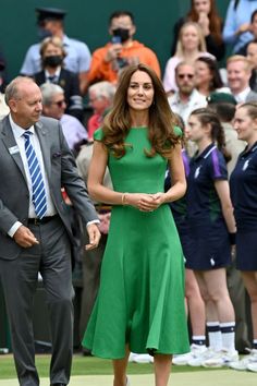 a woman in a green dress is standing on a tennis court while a man in a suit and tie stands next to her