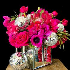 a vase filled with lots of pink flowers and disco balls on top of a wooden table