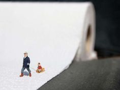 a man and child walking in the snow next to a roll of white paper that is rolled up