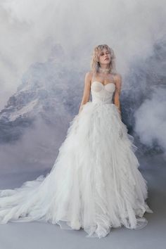 a woman in a white wedding dress standing on a foggy surface with mountains behind her