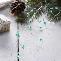 a christmas tree with green lights on it next to a small gingerbread house and pine cones