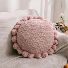 a pink round pillow with pom - poms on top of a white couch