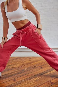 a woman in white top and red pants standing on wooden floor