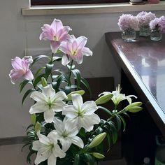 a vase filled with white and pink flowers on top of a wooden table next to a window