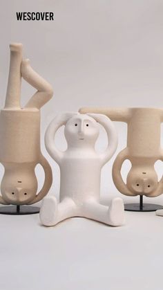 three white vases sitting next to each other on top of black bases with arms and legs in the air