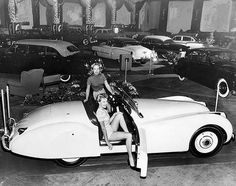 black and white photograph of two women sitting in a car with other cars behind them