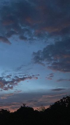 an airplane is flying high in the sky at night with clouds above it and trees below