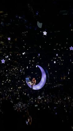 a person sitting on top of a crescent moon in the middle of a dark room