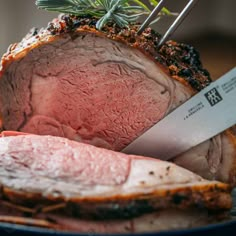 a roast beef on a plate with a knife and rosemary sprig next to it