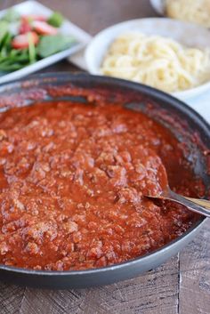 a pan filled with spaghetti and sauce on top of a wooden table next to bowls of salad