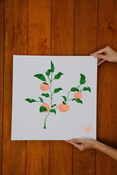 two hands holding up a piece of paper with oranges and green leaves on it