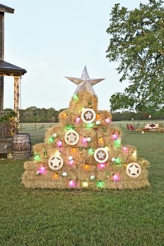 a christmas tree made out of hay with lights and decorations on it in front of a house