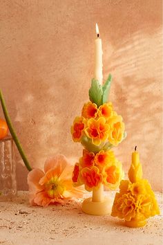 an arrangement of flowers and candles in front of a vase with one candle on it