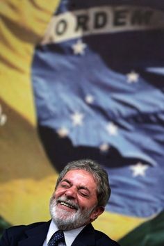 a man in a suit and tie smiles at the camera while standing next to a large flag