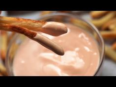 a person dipping some kind of sauce in a glass bowl with pretzel sticks