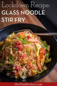 a black bowl filled with noodles and vegetables on top of a wooden table next to a fork