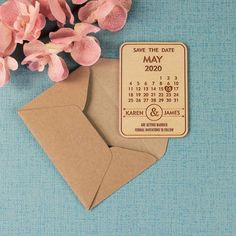 save the date magnets are next to some pink flowers on a blue tablecloth