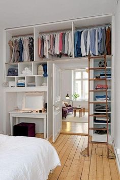 a bedroom with white walls and wooden flooring has open shelving units on the wall