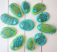 painted rocks with fish on them sitting on a white table next to a wooden wall