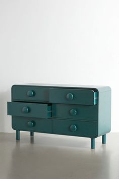 a green dresser sitting on top of a metal floor next to a white wall in an empty room