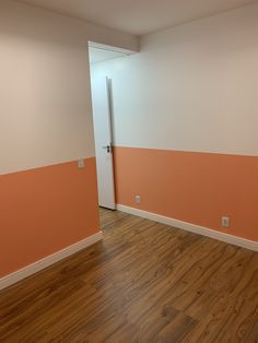 an empty room with hard wood flooring and orange painted walls, along with a white door