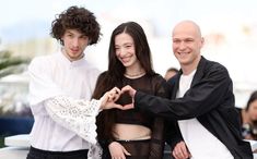 three people standing next to each other making a heart shape with their hands in front of them