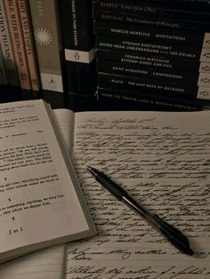 a pen sitting on top of an open book next to a pile of books and papers