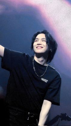 a young man with black hair is holding his hand up in the air and smiling