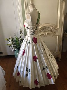 a white dress with red roses on it sitting on a mannequin in front of a mirror