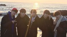 four young men standing next to each other in front of the ocean with one pointing at the camera