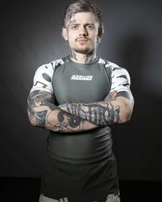 a man with tattoos standing in front of a black background wearing a wet suit and holding his arms crossed