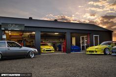 three cars are parked in front of a garage with the sun setting behind them,