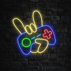 a neon sign with a game controller in the shape of a peace hand on a brick wall