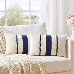 a white couch with blue and white pillows on top of it next to a window