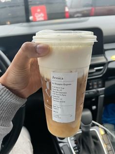 a person holding up a cup of coffee in their hand while sitting in the driver's seat of a car