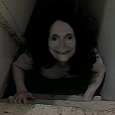 a creepy woman is peeking out from behind a wall with her hands on the ground