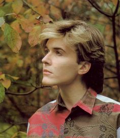 a man standing in front of a tree with leaves on it's branches and looking off into the distance