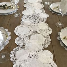 the table is set with white lace doily and place settings on it, along with silverware