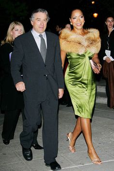 a woman in a green dress walking next to a man wearing a suit and tie