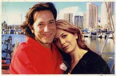 a man and woman posing for a photo in front of the water with sailboats