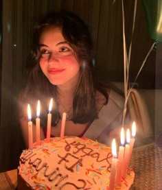 a woman sitting in front of a birthday cake with lit candles