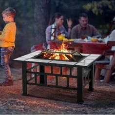 a little boy standing in front of a fire pit with people sitting around the table