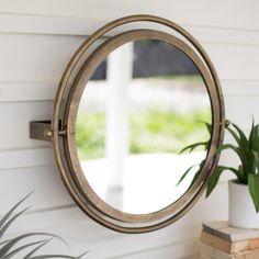 a round mirror hanging on the side of a white wall next to a potted plant