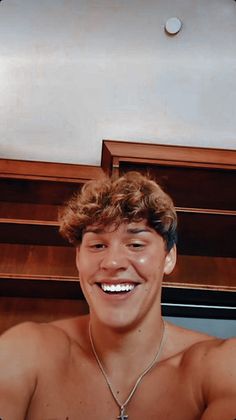 a shirtless young man smiling in front of a book shelf with books on it