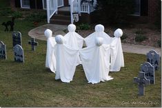 three ghost statues are standing in the grass near headstones and tombstones with white cloth draped over them