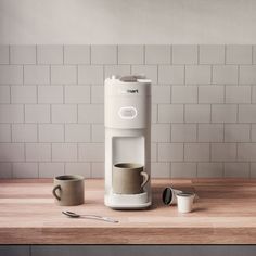 a white coffee maker sitting on top of a wooden counter next to two mugs